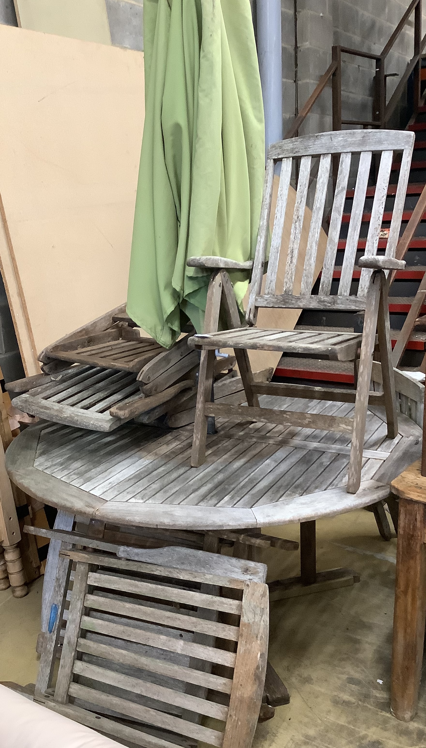 A circular weathered teak garden table, diameter 150cm, height 71cm, a crank parasol and six teak folding elbow chairs